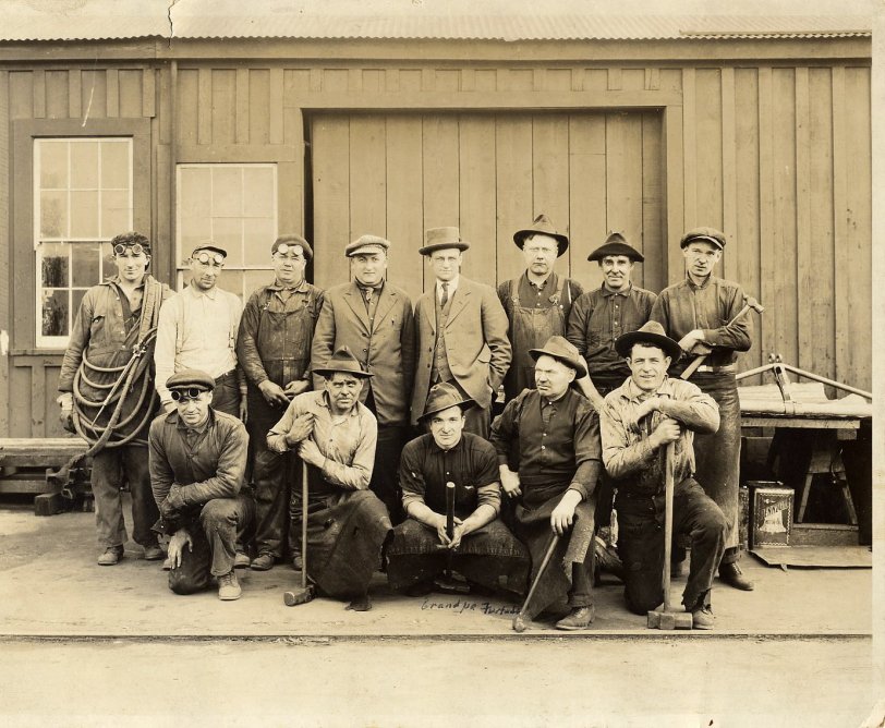 As far as I know, this is a photo of the crew at the Blacksmith Shops for the Southern Pacific Railroad in Oakland, California.  My grandfather (front and center with the rakishly tilted hat) worked for the railroad for some small portion of his life.  His draft card for World War I listed him at the railroad in the blacksmith shop.  By the '30's, he'd started a laundry business elsewhere in Oakland.
He'd emigrated from the Azore Islands to California in around 1915, following other brothers and sisters who'd already left the impoverished islands for the opportunity of the United States.  I can't imagine he was too many years off the boat when this photo was taken, a new immigrant settling into life in California.
I've always liked this, both as a cool posed shot of an industrial shop and by the tools of the trade each worker carries (especially the welder to the far left).  Unlike all the school photos that got saved, it's like every guy in the photo has some emotion on his face, and some story behind it.  Why's the big guy at the right side in the front row look like a superhero, so sure and happy?  What's the Richard Gere look-alike (the welder) thinking?  What's the guy second from the left in the front row staring at off in the distance? View full size.
